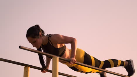 Slow-motion:-a-Beautiful-woman-athlete-doing-push-UPS-on-bars-in-a-black-tank-top-in-great-shape-and-yellow-pants-with-dark-hair.